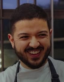 Chef Pedro sorrindo, de avental, na cozinha do Quintal